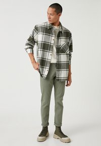 Grön och vit rutmönstrad flanellskjorta med bröstficka, kombinerad med olivgröna slim-fit byxor och tanfärgade snörskor. Slät textur.