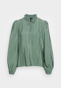 Blusa verde feita de tecido brilhante, com um decote alto com babados, mangas longas bufantes e detalhes em renda nas laterais.