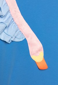 Bright blue shirt featuring a textured light blue ruffle and a pink fabric detail resembling a duck's neck, with an orange and yellow beak.