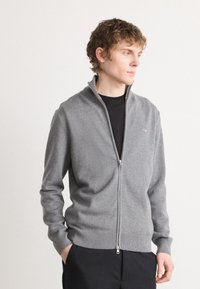 Gray zip-up cardigan made of soft knit fabric, featuring a ribbed hem and cuffs, with a small logo detail on the chest.