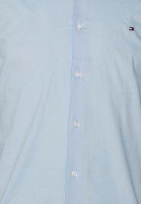 Hellblaues Hemd mit Knöpfen aus Baumwolle mit glatter Textur. Verfügt über weiße Knöpfe und ein kleines gesticktes Logo auf der Brust.