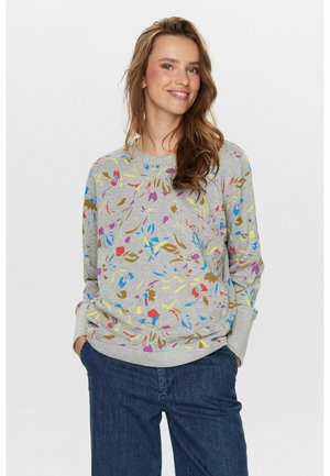 Szary sweatshirt z wielokolorowym wzorem kwiatowym; ma długie rękawy, okrągły dekolt oraz ściągacze na rękawach. W połączeniu z ciemnoniebieskimi dżinsami.