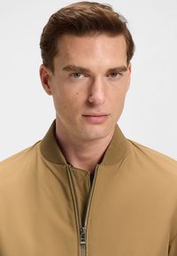 Pruun pommitajate jope soonikkoelise krae, eesmine tõmblukk ja sile tekstuuriga. Omadused: ühtlane värv ilma mustrite või aksentideta.