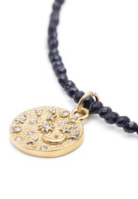 Vedhæng i guldfarvet metal med tekstureret overflade, dekoreret med klare rhinsten og en månesegl, på en mørkeblå perlehalskæde.