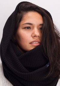 Black knitted infinity scarf with a textured pattern, worn loosely around the neck, featuring a subtle label detail.