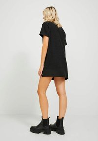 Black short-sleeve dress with a relaxed fit, made from a textured material, featuring a below-hip length. Paired with black ankle boots.
