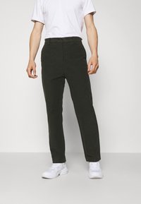 Dark green trousers made of soft fabric, featuring a straight cut, front pockets, and a button closure. Worn with a white T-shirt and sneakers.