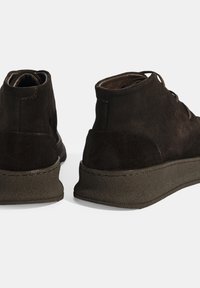 Bruine suède enkelboots met een gestructureerde rubberen zool, met een ronde neus en minimale stikdetaillering. Veters aan de voorkant.