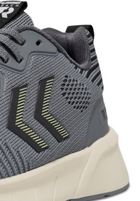 Grauer Sportschuh mit einem strukturierten Stoffobermaterial und reflektierenden, hellgrünen Akzenten, einer gepolsterten Sohle und einer Zuglasche an der Ferse.