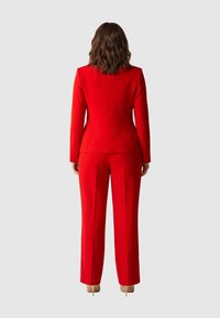 Roter maßgeschneiderter Anzug mit strukturierter Blazerjacke und geraden Hosenbeinen. Glatter Stoff mit leichtem Glanz, der eine taillierte Silhouette und lange Ärmel aufweist.