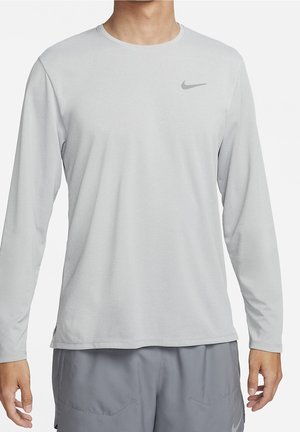 Man draagt lichtgrijs, sportief shirt met lange mouwen en bijpassende grijze short met Nike-logo's op borst en short.