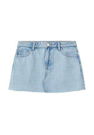 Jeune femme aux longs cheveux blonds porte un top marron décolleté, une mini-jupe en denim bleu clair et des ballerines marron, debout devant un fond blanc.