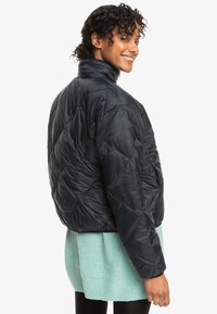 Dark blue puffer jacket with a high collar, diamond quilted pattern, and a lightweight finish, worn over a mint green sweater.
