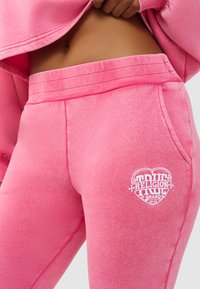 Roze joggingbroek gemaakt van een zachte katoenmix met een geribde tailleband, zijzakken en een wit "True Religion" hartlogo detail.