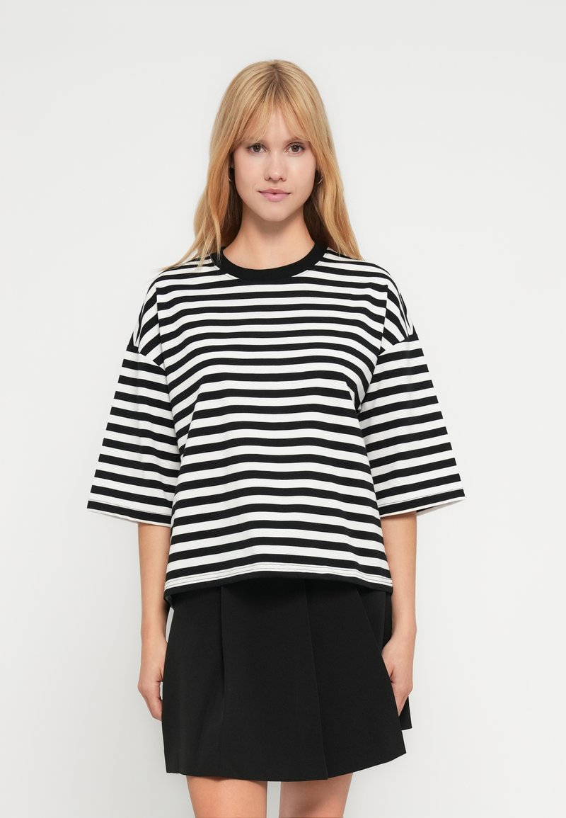 Μπλούζα με κοντά μανίκια σε ασπρόμαυρες ρίγες και στρογγυλή λαιμόκοψη, με χαλαρή γραμμή και μαύρη φούστα στο κάτω μέρος.