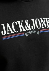 Μαύρο ύφασμα με λευκό κείμενο "JACK & JONES", κόκκινες και μπλε οριζόντιες γραμμές και "19 ORIGINALS 90" σε μια μικρή σημαία από κάτω.