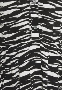 Black and white dress featuring a zebra stripe pattern, buttoned front with metallic buttons, and gathered fabric at the waist.