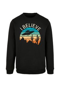 Schwarzer Sweatshirt mit einem grafischen Druck eines UFOs vor einem mehrfarbigen Sonnenuntergang mit Bergen und Kakteen, der Text lautet "ICH GLAUBE."