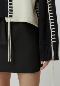 Un pull en tricot noir et crème avec des poignets côtelés et des coutures découratives crème sur les côtés ; associé à une jupe noire.