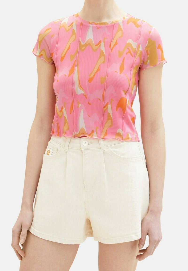 Top corto de manga corta rosa con patrones ondulados en naranja y blanco. Combinado con pantalones cortos de mezclilla de color claro con un sol bordado en el bolsillo.