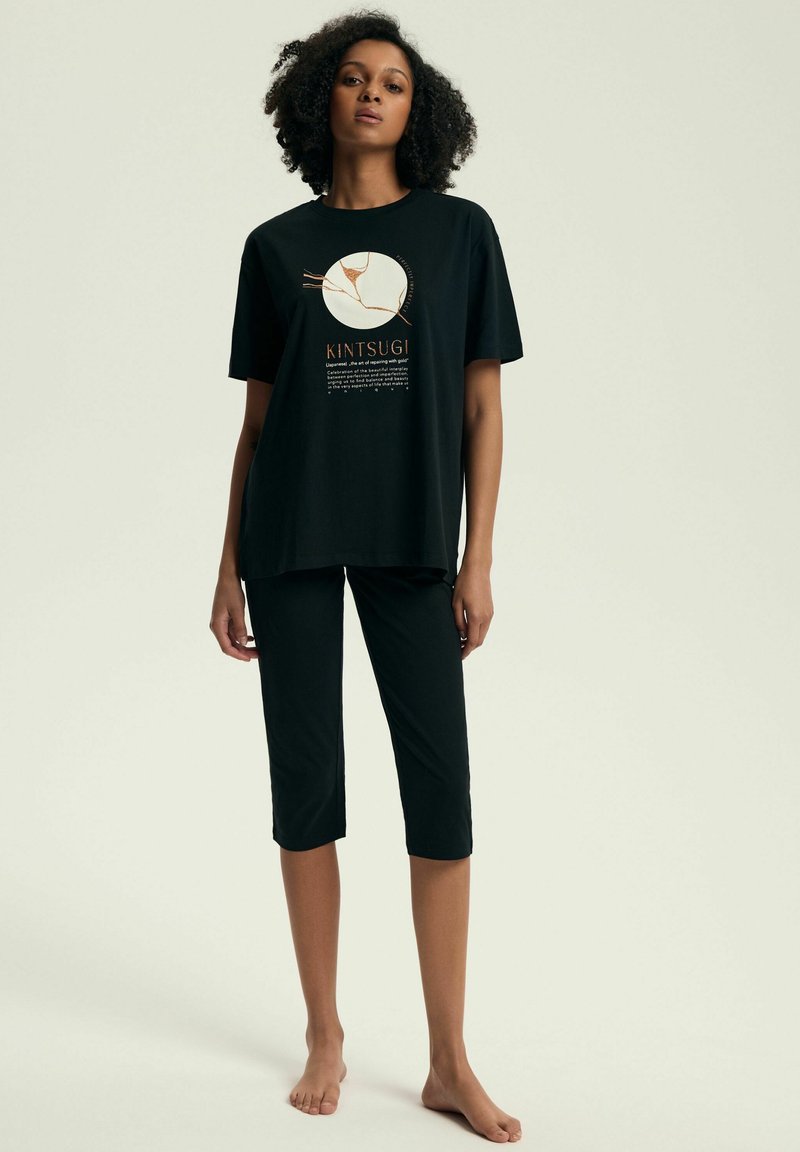 Czarny bawełniany t-shirt z krótkim rękawem, ozdobiony grafiką Kintsugi. Do tego czarne krótkie spodnie, całość casualowa i wygodna.