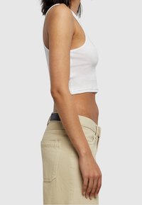 Débardeur blanc court en coton, associé à un pantalon beige. Le débardeur présente un col rond et un design sans manches avec une texture lisse.