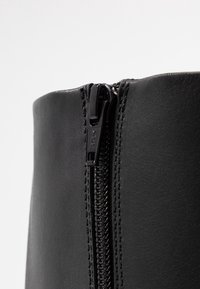 Stivale alla caviglia in pelle nera con zip laterale, dotato di etichetta YKK, texture liscia e design strutturato.