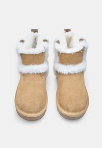 Botas de tobillo de ante en color marrón con dobladillo de piel sintética blanca, puntera redondeada y suela de goma plana. Incluye dos pequeños detalles en forma de bucle en el puño.