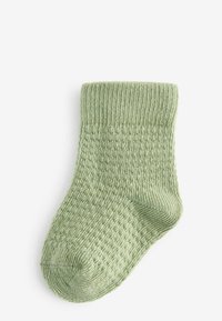 Grøn strikket sok med et tekstureret mønster, ribbede kanter og en rund tå. Materialet ser blødt og hyggeligt ud.