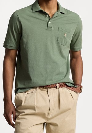 Zielona bawełniana koszulka polo z kołnierzykiem, krótkimi rękawami i kieszonką na piersi z małym logo. Do tego jasnobeżowe spodnie khaki i pleciony pasek.
