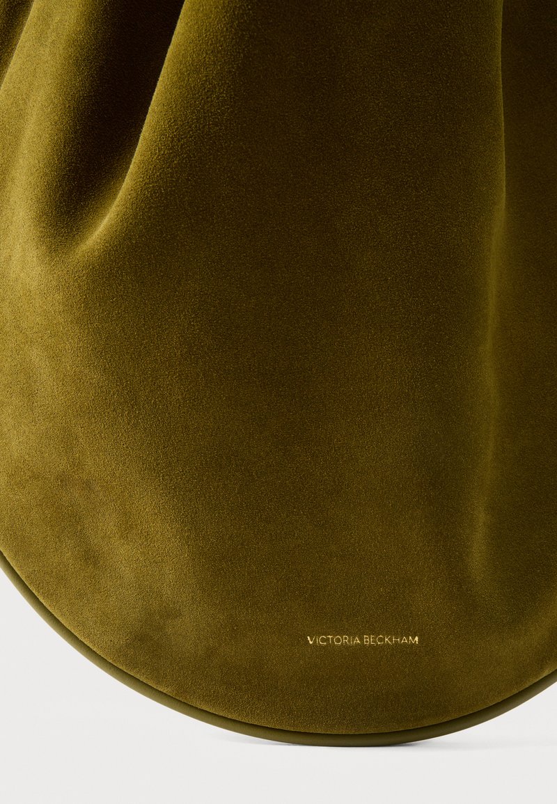 Sac à main en daim vert olive avec fond courbe et logo "Victoria Beckham" embossé en or près de la base sur fond blanc.