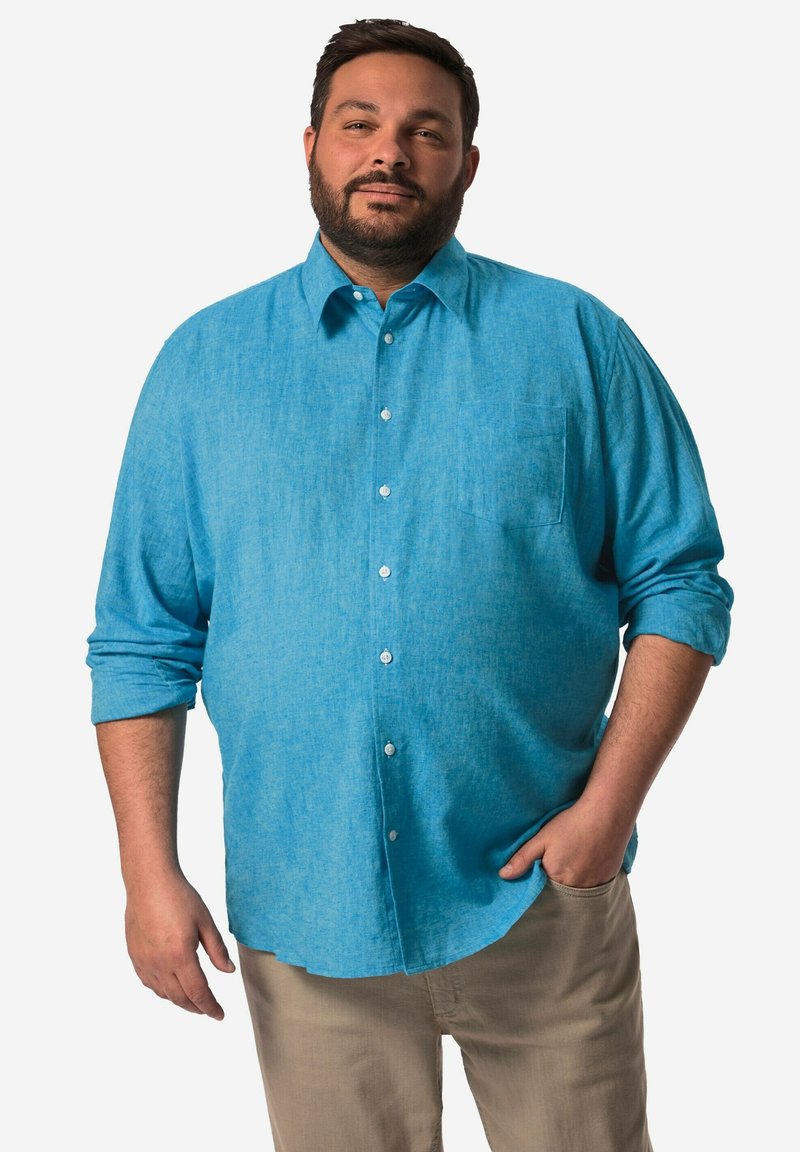 Světle modrá košile na knoflíky z jemné, texturované látky. Má jednu náprsní kapsu a ohrnuté rukávy. V kombinaci s béžovými kalhotami.