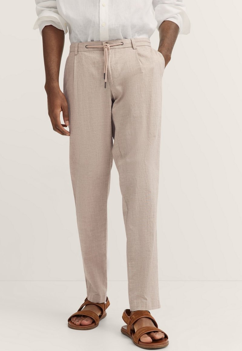 Helle beige Leinenhose mit lockerer Passform, Kordelzugbund und glatter Textur, kombiniert mit braunen Sandalen mit doppelten Riemen.