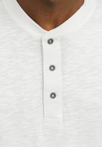 Fehér, rövid ujjú henley ing texturált anyagból, lekerekített gallérral és három fekete gombbal a záráshoz.