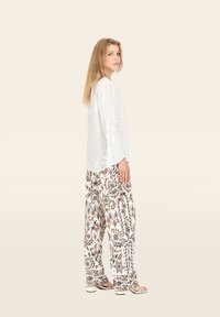 Blusa bianca oversize con dettagli tessurizzati abbinata a pantaloni a gamba larga marroni e crema con motivi floreali.
