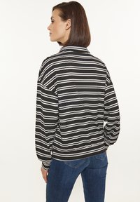 Maglione a righe bianche e nere con colletto alto, tessuto strutturato e vestibilità ampia. Il retro ha un orlo arrotondato, abbinato a jeans blu.
