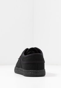 Sneaker in tela nera con suola in gomma nera testurizzata, forma arrotondata e dettagli di cucitura sottili. Presenta un colletto imbottito per maggiore comfort.