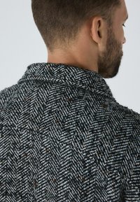 Sako s vzorom rybí chvost v čiernej a bielej farbe, s textúrovanou tkaninou, golierom a viditeľnými švovými detailmi. Zobrazený zadný pohľad.