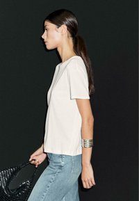 Hvid kortærmet t-shirt med rund halsudskæring, parret med lyseblå denim jeans og en sort vævet taske. Sølv cuff armbånd på håndleddet.
