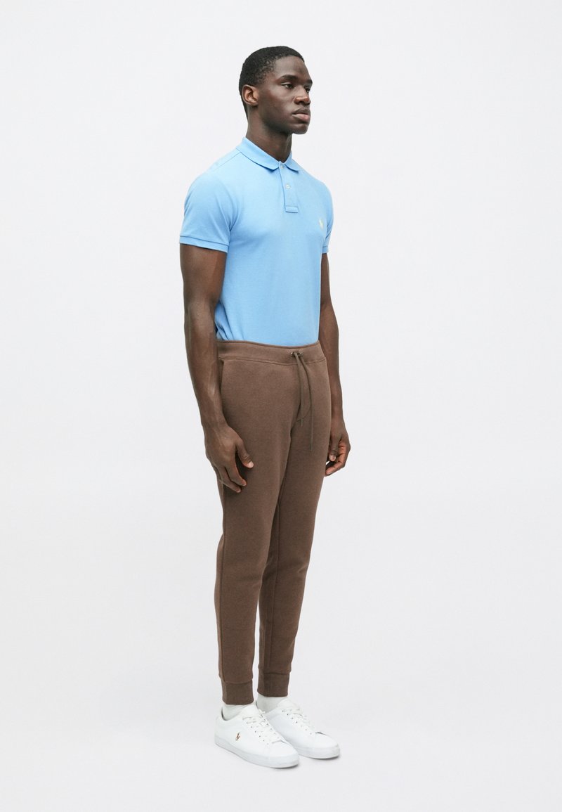 Hellblaues Polohemd mit kurzen Ärmeln und Kragen, kombiniert mit braunen Jogginghosen und weißen Turnschuhen. Einfaches Design, lässige Passform, weiche Texturen.