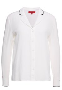 Witte blouse van zachte stof, met een klassieke kraag, zwarte bies langs de kraag en manchetten, en lange mouwen.