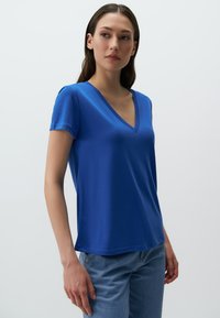 Niebieska koszulka z dekoltem w serek, krótki rękaw, miękka tkanina, luźny krój; w połączeniu z jasnoniebieskimi dżinsami, o prostym kroju i minimalnych detalach.