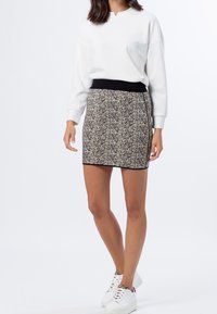 Haut blanc à manches longues avec un petit col en V, associé à une jupe à motifs noir et crème, et des baskets blanches à lacets.
