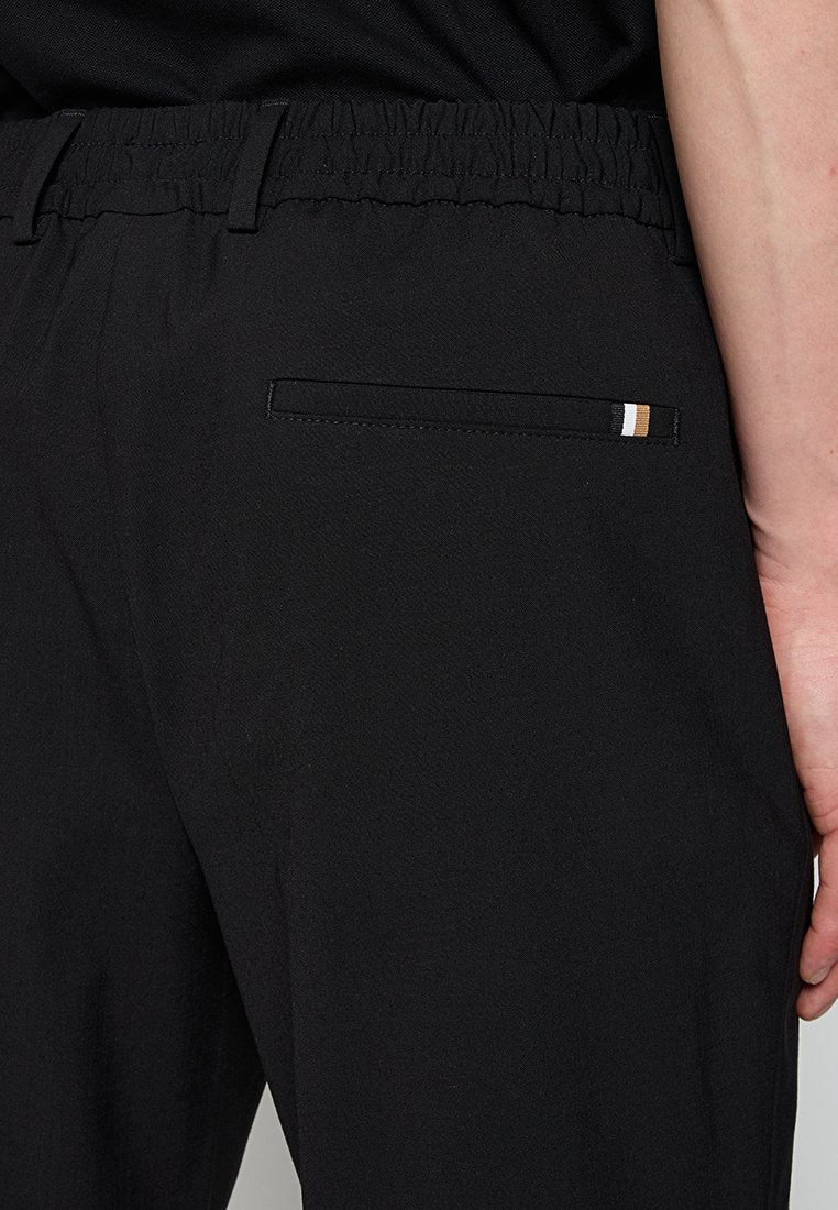 Pantalon noir avec une taille élastique, doté d'une poche arrière avec un accent à rayures étroites en tan et blanc, fabriqué en tissu texturé.