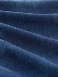 Tela de mezclilla azul oscuro, con una textura suave y sutiles variaciones de tono, dispuesta en pliegues suaves y fluidos.