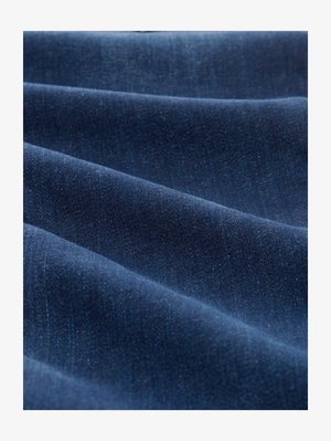 Donkerblauwe denimstof met een gladde textuur en subtiele kleurvariaties, gerangschikt in zachte, vloeiende plooien.