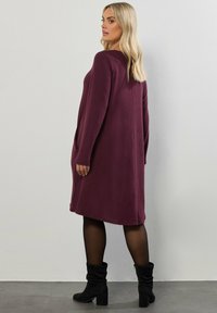 Długa sukienka z długim rękawem, do kolan, w głębokim burgundowym kolorze, z bocznymi kieszeniami i luźnym, wygodnym krojem. Noszona z czarnymi, wysokimi kozakami.
