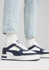 Witte en marineblauwe sneakers met glad leren en textielen bovenzijde, voorzien van een dikke witte zool, veters en gouden logo-accenten.