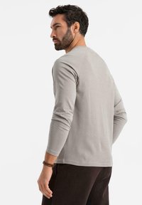 Vaaleanharmaa pitkähihainen paita, jossa on istuva muotoilu, ribatoitu pinta ja pyöreä kaula-aukko. Yhdistetty tummanruskeisiin housuihin, nähtynä takaa.