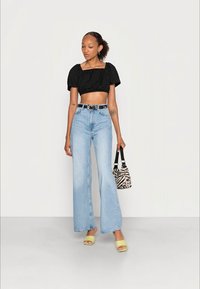 Camiseta preta cropped, jeans de cintura alta azul claro, sandálias verde de slide e uma pequena bolsa de zebra. Texturas suaves, design casual.